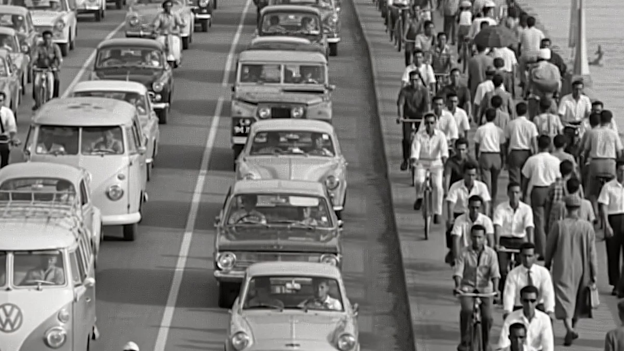 Dense traffic and crowds of cyclists and pedestrians on a Lagos road, mid twentieth century